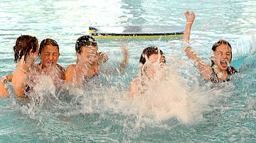 Eine Gruppe Kinder im Wasser, im Vordergrund spritzt viel Wasser nach oben, der Hintergrund ist unscharf. 