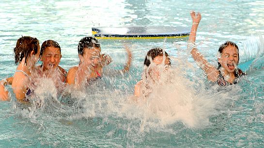 Eine Gruppe Kinder im Wasser, im Vordergrund spritzt viel Wasser nach oben, der Hintergrund ist unscharf. 