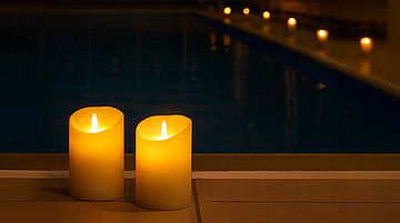 Zwei brennende Kerzen am Beckenrand einen Hallenbads, im Hintergrund weitere brennende Kerzen als Symbolbild für Das Kerzenschwimmen 2025 im Stadtbad Schwerte