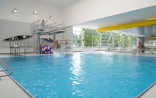 Innenansicht des Stadtbad Schwerte. Zu sehen ist das Sprunbecken mit drei Sprungtürmen und Kindern, die ins Wasser springen.
